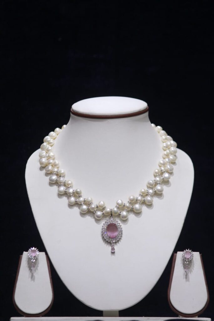 Three-layered pearl necklace set with pink stone pendant, showcasing elegant and vibrant design.