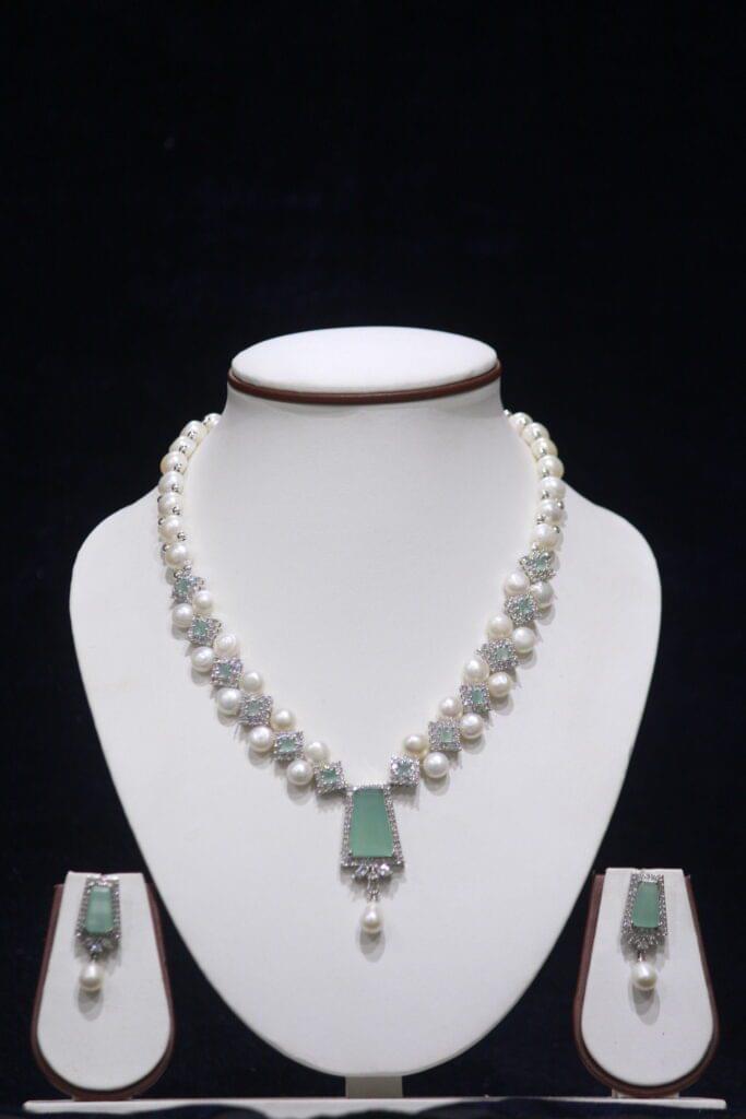 Elegant pearl necklace set featuring a striking green stone pendant, with matching earrings, offering a sophisticated and timeless design.