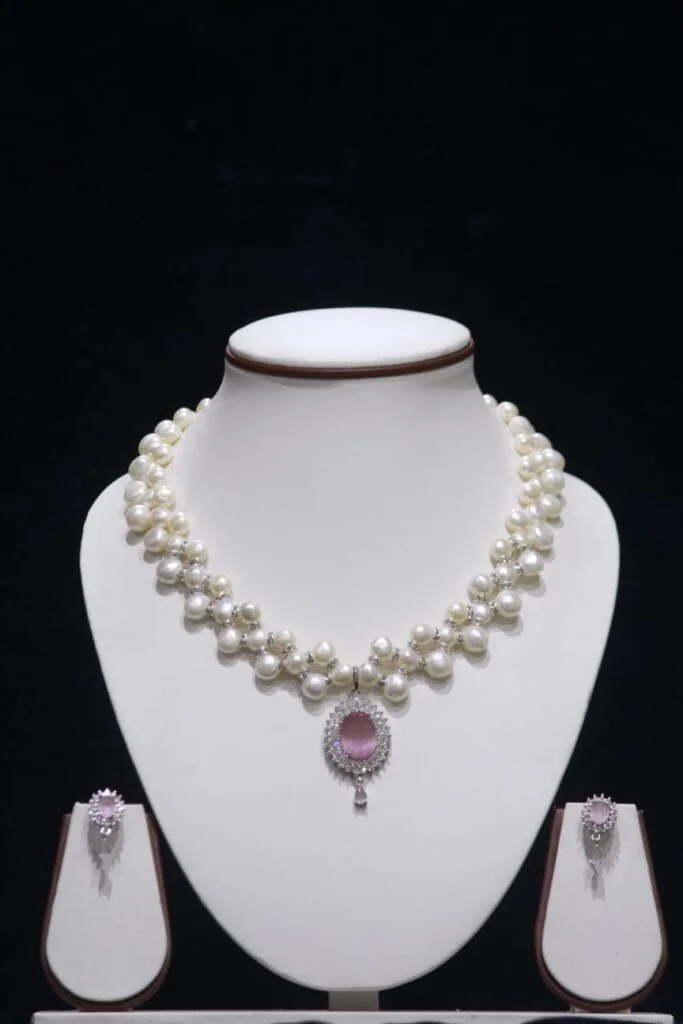 Three-layered pearl necklace set with pink stone pendant, showcasing elegant and vibrant design.